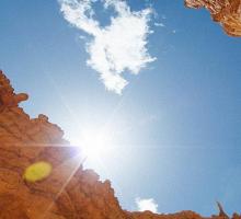 Canyon walls with the sun overhead and a small cloud in the sky