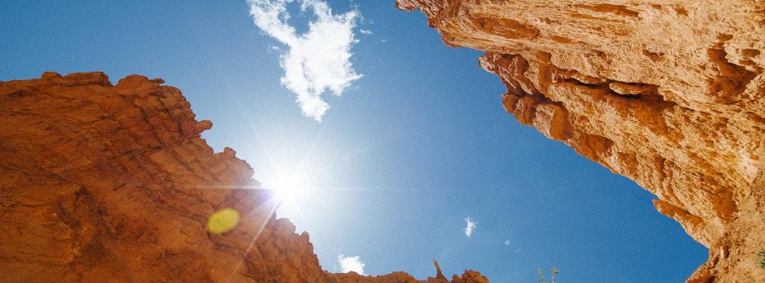 Canyon walls with the sun overhead and a small cloud in the sky